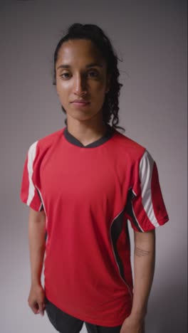 Vertical-Video-Studio-Shot-Of-Female-Footballer-Wearing-Club-Kit-Against-Grey-Background-Catching-Ball